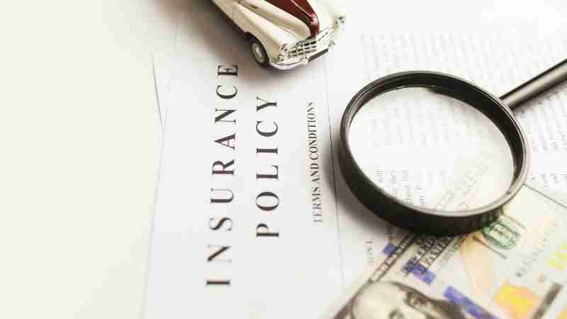 Close-up image of an insurance policy with a magnifying glass, money, and toy car., tags: zu - pexel